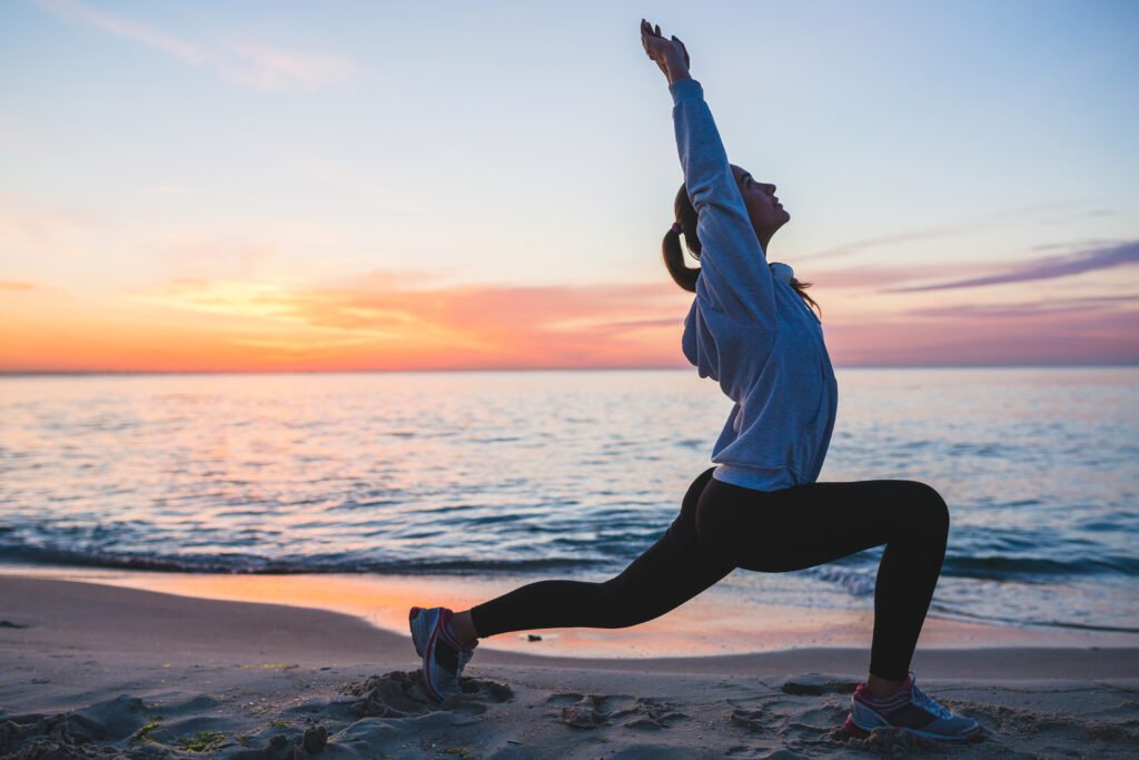 young woman doing sport exercises on sunrise beach in morning, stretching, healthy lifestyle, yoga